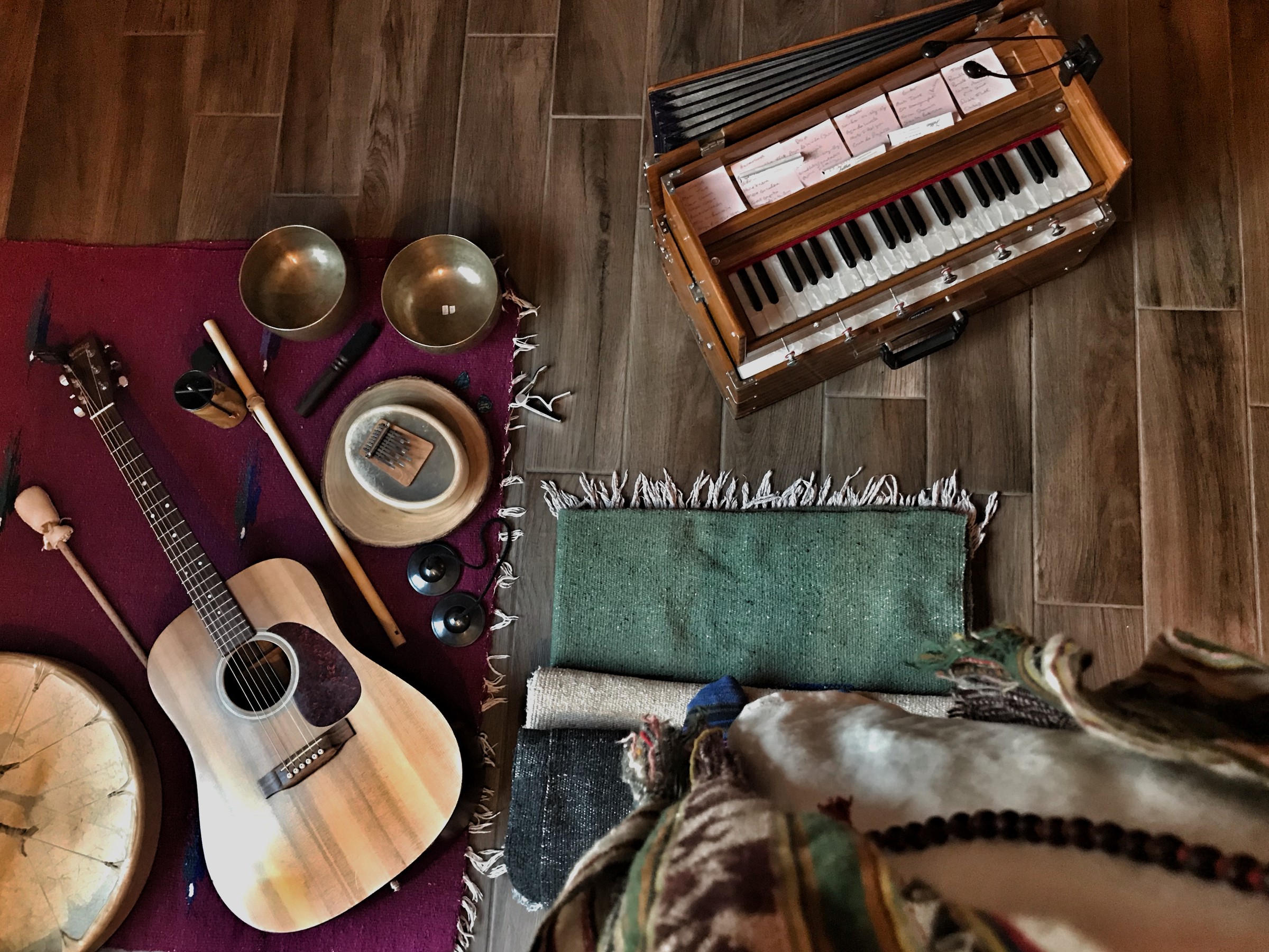 A guitar, two metal bowls, mallets and a harmonium laid out on rugs on a wooden floor
